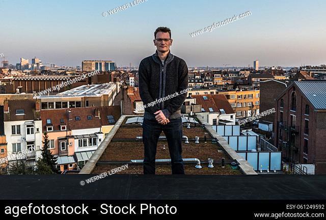 Tall forty year old man standing on his roof, overlooking the Brussels skyline, Jette, Brussels, Belgium