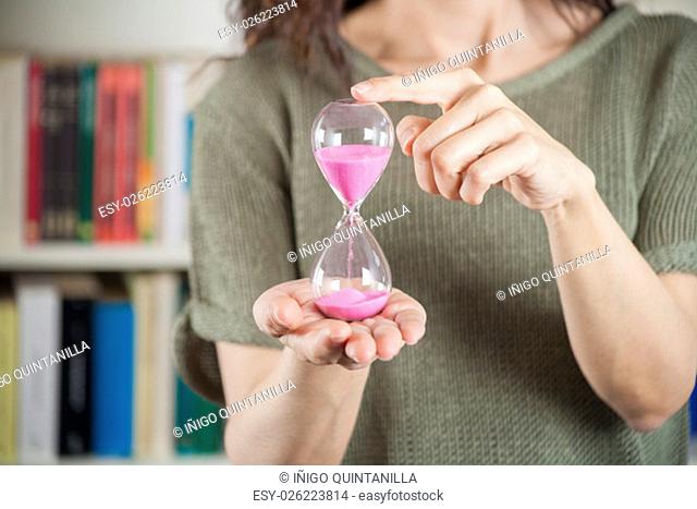 pink sand clock in woman hands over library background
