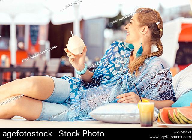 Young smiling woman leaning on pillow enjoying coconut water