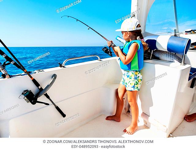 Lovely little girl with a fishing rod fishing from the boat