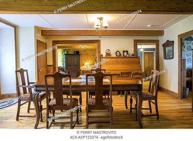 Dining room with antique wooden table and upholstered high-back chairs, roll top desk inside an old circa 1752 Canadiana style fieldstone house, Quebec, Canada