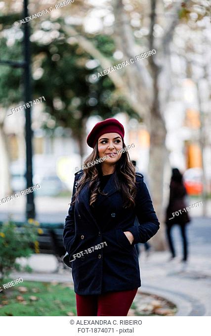 Smiling young woman in beret walking in urban autumn park