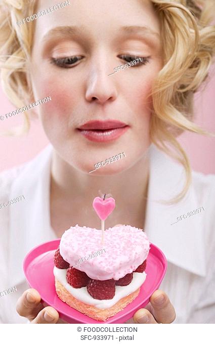 Young woman blowing out candle on raspberry cake