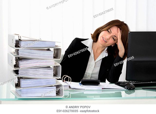 Stressed Young Businesswoman Looking At Stack Of Folders In Office