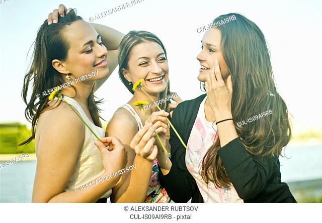 Three young female friends on riverbank holding dandelions