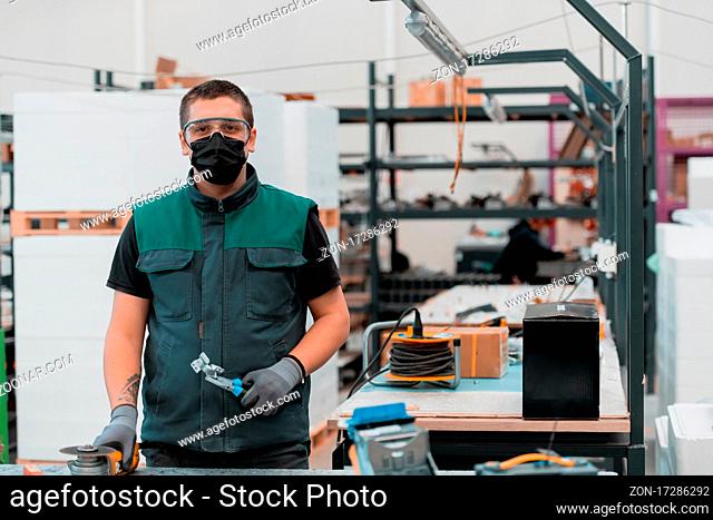 Heavy Industry Engineering Factory Interior with Industrial Worker Using Angle Grinder and Cutting a Metal Tube.He Wears a Mask on His Face Because of the...