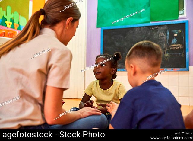 Kindergärtnerin und zwei Kinder reden und spielen zusammen im internationalen Kindergarten