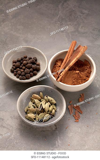 Three dishes of spices: allspice, cardamom and cinnamon