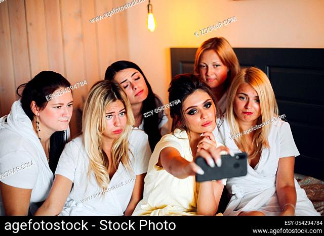 Group of pretty ladies with a bride in the middle in white taking selfie. They are having a hen party in a hotel or relaxing in spa
