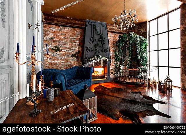 Interior with fireplace, candles, skin of cows, brick wall, large window and a metal cell of a loft, living room, coffee table and dark blue sofa in modern...