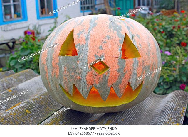 Orange pumpking with cut face is ready for Halloween on rural house background. Halloween in village. Pumpkin symbol of Halloween