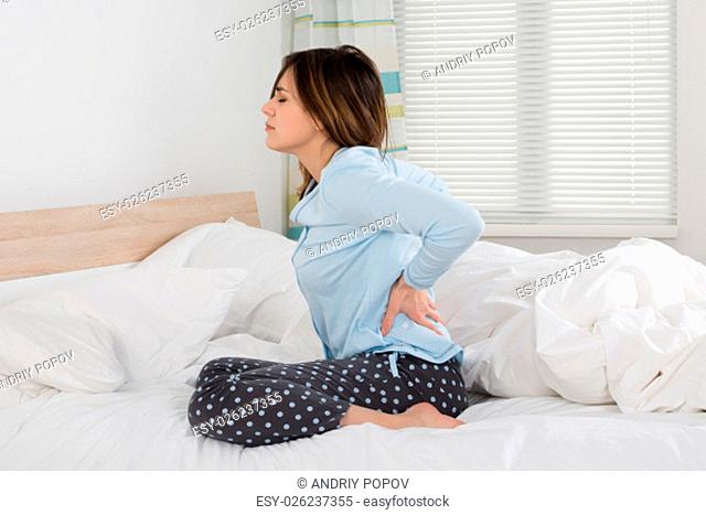 Woman Suffering From Back Pain Sitting On Bed