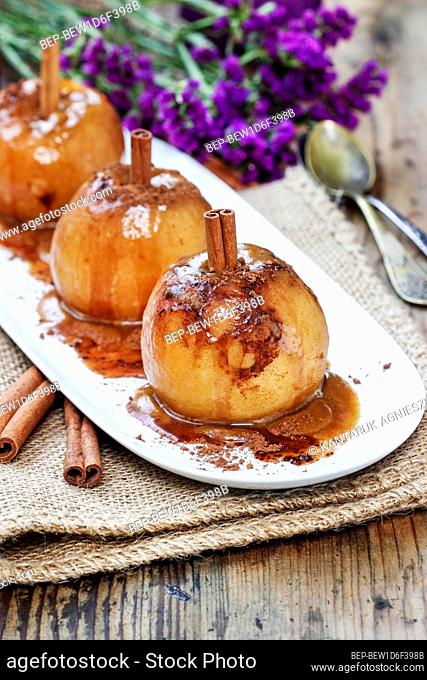 Apples in caramel. Plate standing on beautiful wooden table, violet decorations and scented candles in the background