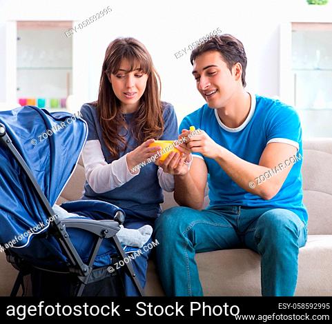 Young parents with their newborn baby in baby pram sitting on the sofa