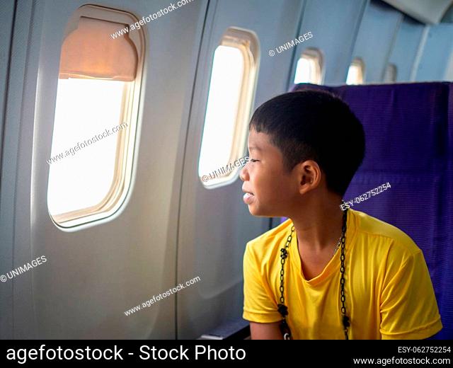 An Asian boy sits and smiles and looks out the window of an airplane