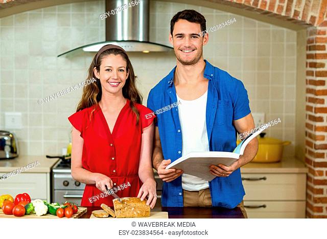 Portrait of woman cutting loaf of bread and man checking recipe book