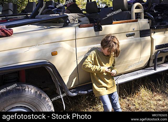 Eight year old boy leaning against a jeep, playing with a toy
