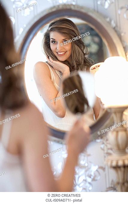 Portrait of young woman looking in wall mirror
