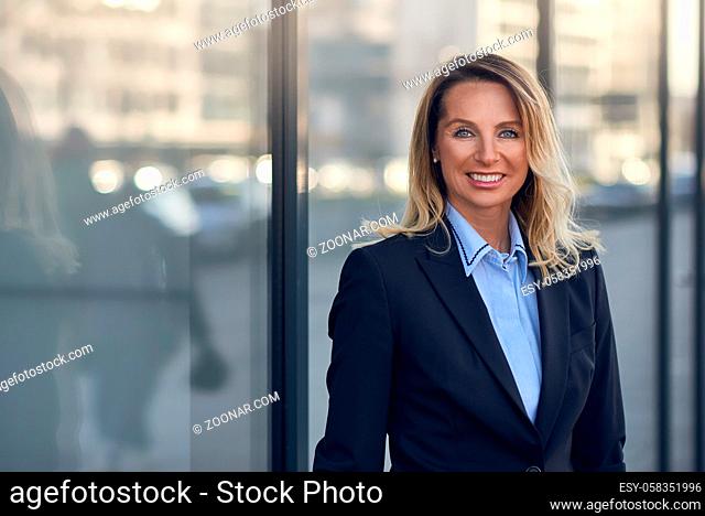 Smiling businesswoman standing in front of a large glass window on a commercial building in town with reflection and copy space