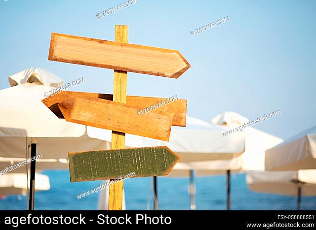 Wooden pointer post with copy space at the beach. arrows on a guidepost pointing at the sea. Signpost showing the way to the beach resorts in front of white...