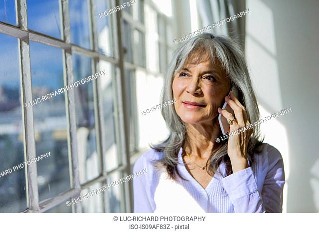 Senior woman looking out of window whilst using smartphone