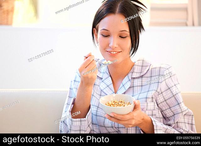Young smiling woman having cereal breakfast in pyjama