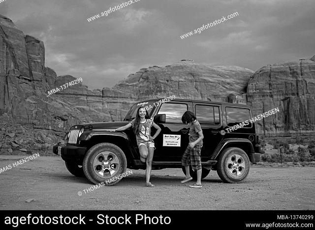 A girl and a boy in front of a Jeep Wrangler and a classic view of Monument Valley from Artist Point. Monument Valley Navajo Tribal Park, Utah and Arizona, USA