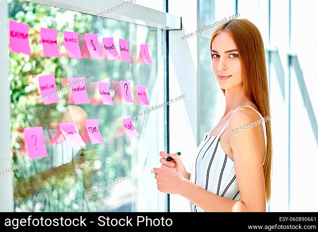 Attractive confident business woman using sticky notes to write and share ideas in creative office. business, people, teamwork and planning concept
