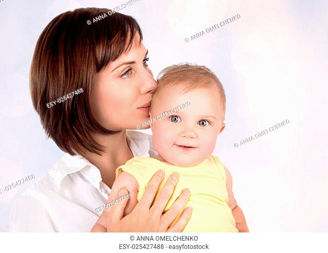 Portrait of beautiful gentle mother kissing her precious little baby over blur background, young loving family, enjoying motherhood