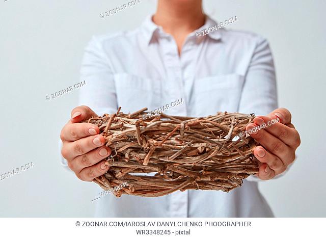 A girl in a white shirt gives an empty nest of branches, isolated on a gray background. Easter