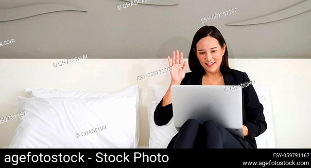 Asian woman in black suit use the laptop computer to work in the morning in bed. Waved her hand over the wireless communication on laptop computer screen