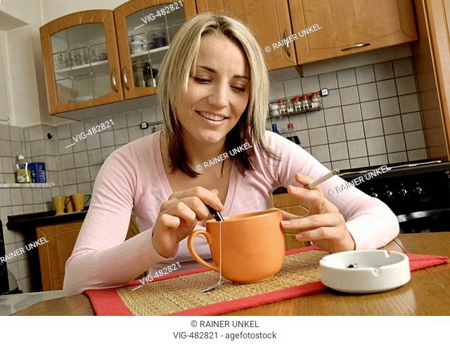 GERMANY : Young woman with a cigarette drinking a cup of tea in her kitchen . - Koeln, GERMANY, 24/07/2007