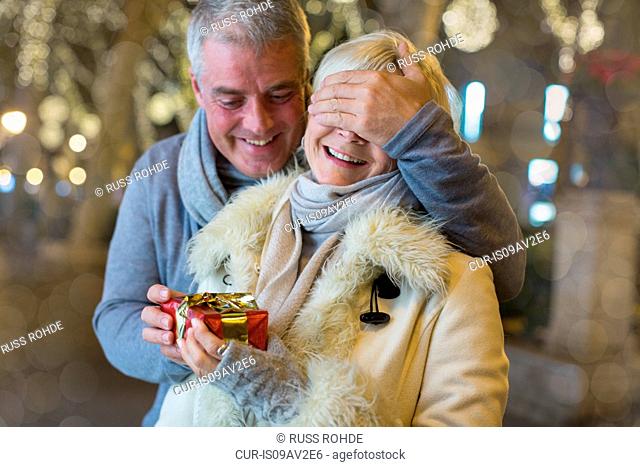 Mature man handing with xmas gift to wife on tree lined avenue, Majorca, Spain