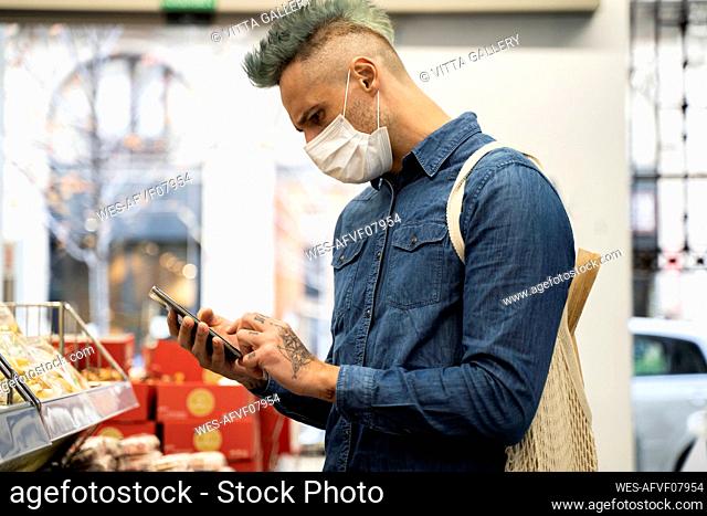 Stylish man wearing face mask using smart phone in supermarket