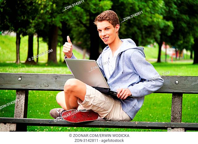 Ein Teenager mit Laptop im Freien. Sitzt im Park. Mobiles Internet
