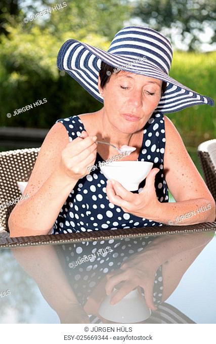 attractive woman siiting by the pool and eating a bowl of fruit