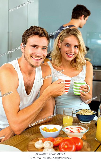 Smiling young couple holding coffee cups at home