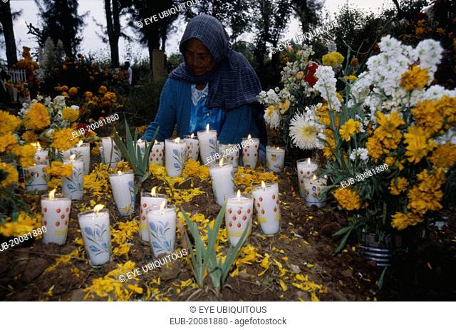 Tarascan Indian woman lighting candles on grave decorated with marigold flowers for Night of the Dead in Tzintzuntzan Cemetery
