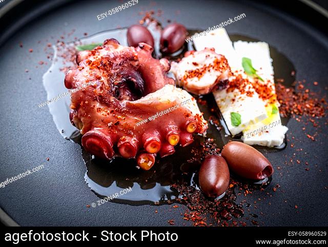 Modern style traditional Greek chtapodi scharaswith barbecued octopus, olives and feta cheese offered as close-up on a Nordic design plate