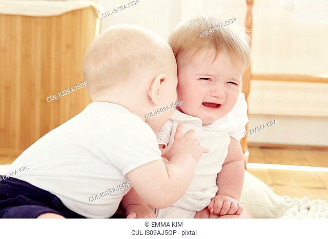 Crying baby girl with baby boy leaning toward her