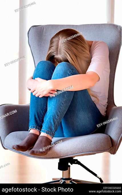 Sad girl is sitting on a chair at home