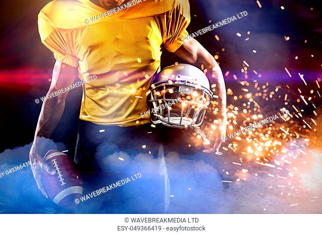 Mid section of male athlete with American football and helmet against firework bursting sparkle background