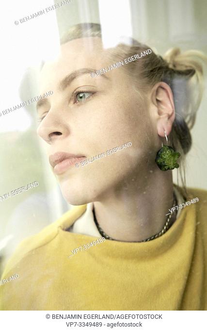 young wistful woman wearing earring made of raw zucchini, looking away into distance