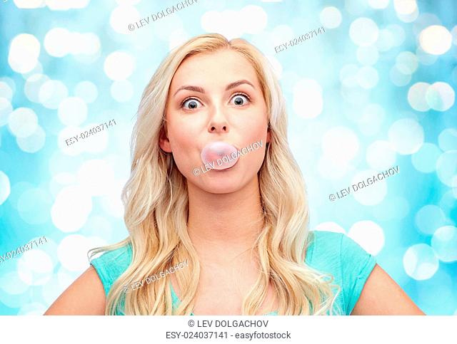 emotions, expressions and people concept - happy young woman or teenage girl chewing gum over blue holidays lights background