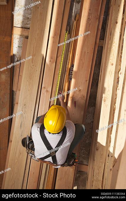 Mixed race construction worker measuring lumber