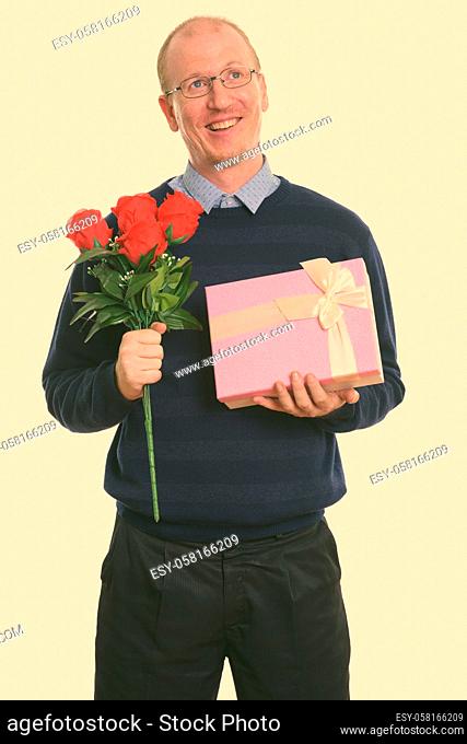 Thoughtful happy man smiling while holding red roses and gift box ready for Valentine's day