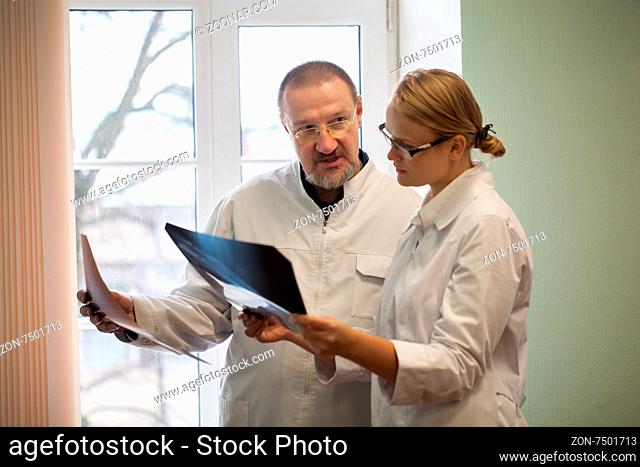 Professor and young female doctor examining and comparing two x-ray images standing by the window in clinic