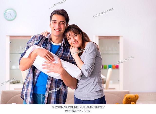 Young parents with their newborn baby near bed cot