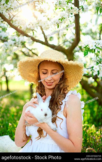 The beautiful girl with white rabbit in the blossoming apple-trees garden. White flowers in a garden in sunshine. Spring apple trees in blossom