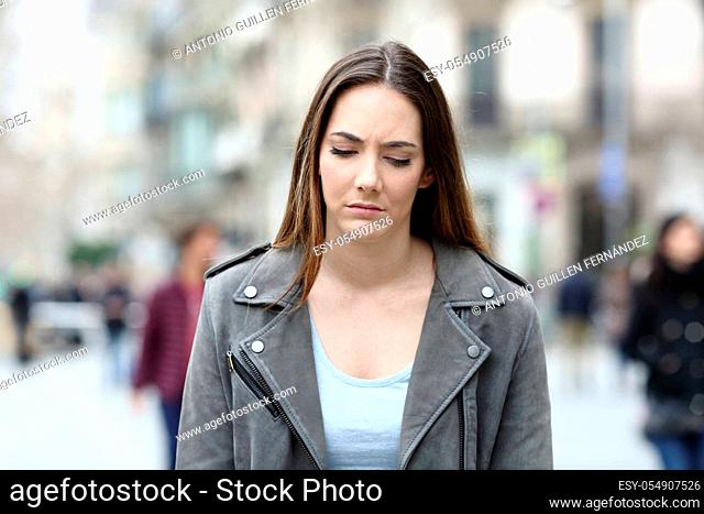 Front view portrait of a depressed young woman walking on city street